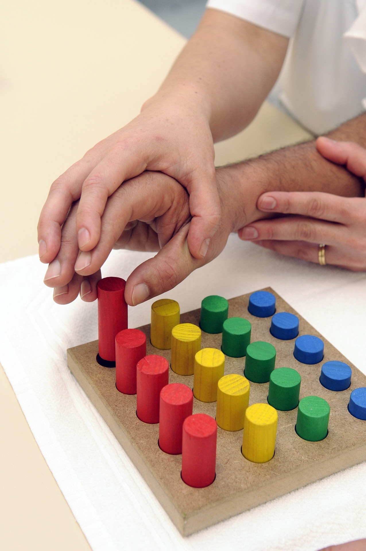 Ergotherapeutin führt die Hand einer Patientin beim Feinmotorik- und Wahrnehmungstraining mit bunten Holzstiften